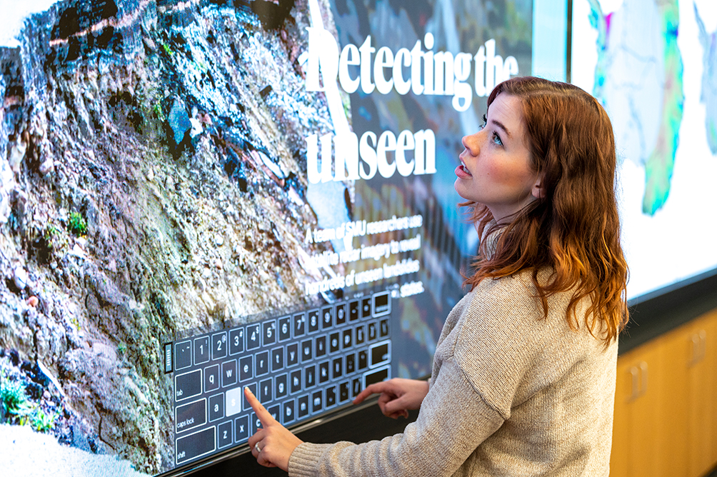 A person looks up at a large digital screen while typing on a virtual keyboard